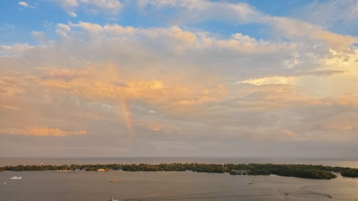 A rainbow with multi-coloured clouds over an island and busy small harbour