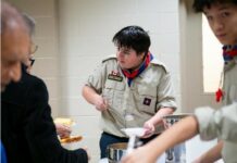 Serving with Joy: Explorers and Seniors Unite at St. Thomas the Apostle Parish A young explorer serves senior parishioners in a Church hall
