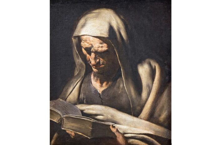 A cowled old-Testament prophet reads scripture in a mysterious half-light