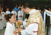 Holy Communion Prayer A young girl in a white alb receives First Holy Communion from a smiling priest