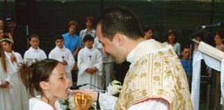 Holy Communion Prayer A young girl in a white alb receives First Holy Communion from a smiling priest