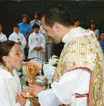 Holy Communion Prayer A young girl in a white alb receives First Holy Communion from a smiling priest