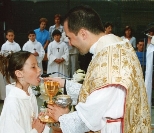 Holy Communion Prayer A young girl in a white alb receives First Holy Communion from a smiling priest
