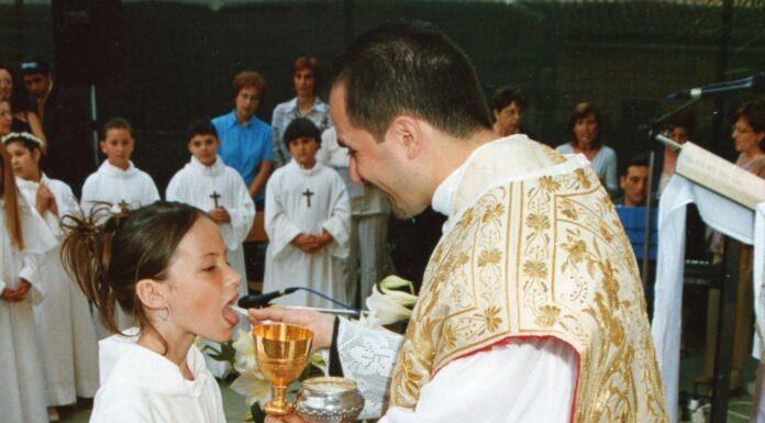 Holy Communion Prayer A young girl in a white alb receives First Holy Communion from a smiling priest